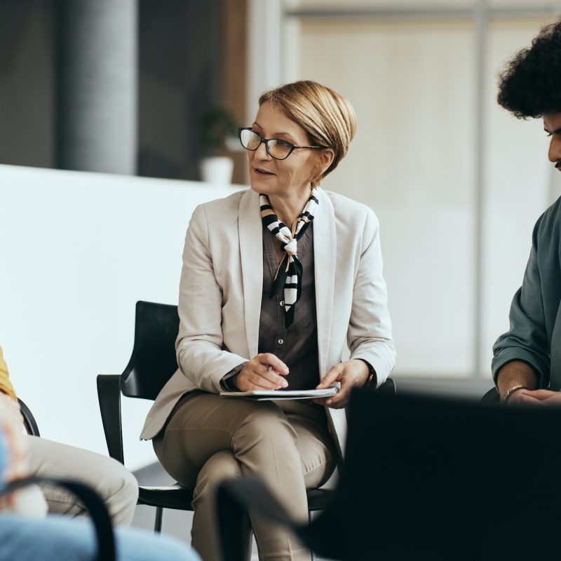 mature-therapist-talking-to-participants-of-group-therapy-at-mental-health-center-.jpg
